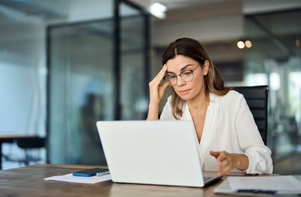 Focused individual experiencing digital eye strain while working on a laptop in a modern office setting