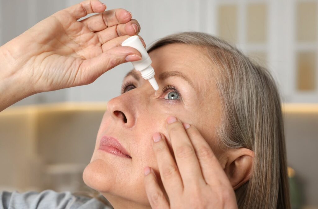 A person looks up at the ceiling as they squeeze prescription eye drops into their eyes to help with dry eye symptoms.
