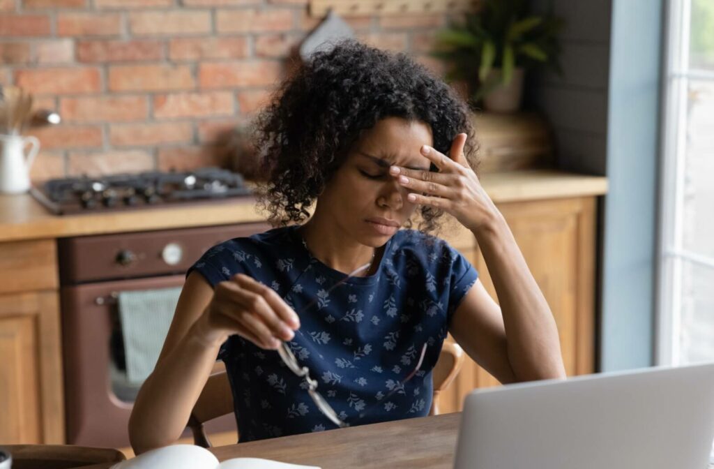 A person sitting in front of a laptop while holding their forehead, appearing to have a headache.