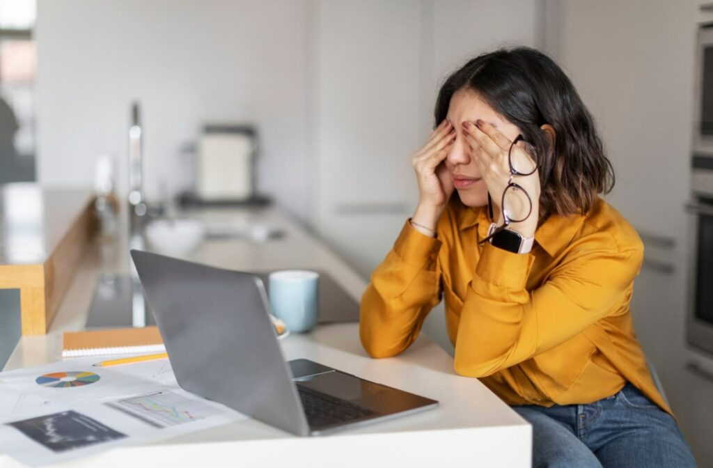 Woman rubbing her eyes while sitting in front of a laptop, showing signs of digital eye strain.